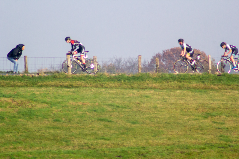 Four cyclists are riding up a grassy hill in the Netherlands during a race.