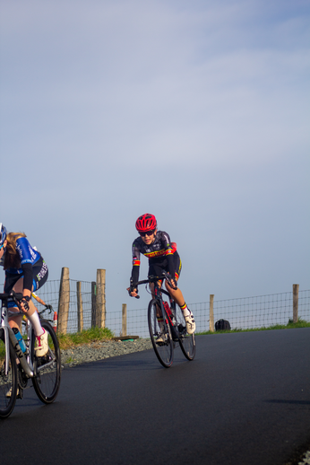 Two women are riding bikes down a road under a blue sky.