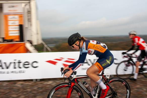 A young woman wearing a blue and orange cycling outfit is riding her red and black bicycle down the street.