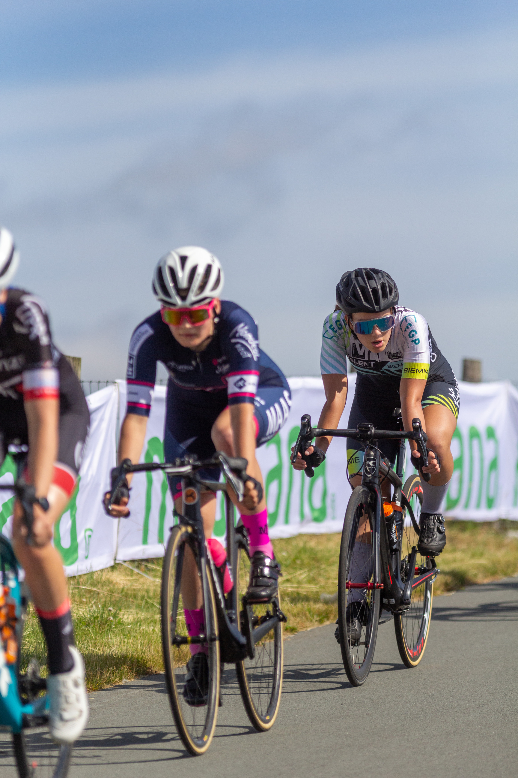 Two women on bikes race against each other, one of them wearing a blue jersey with the word "land".