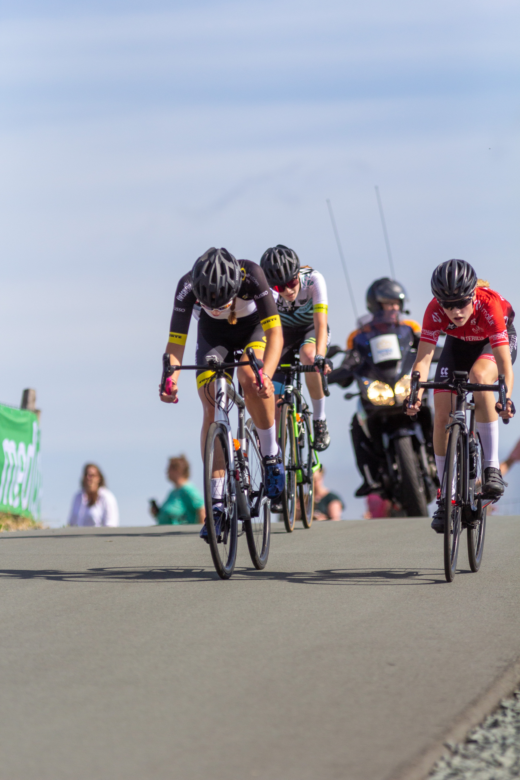 Three women are riding bikes down a hill, all wearing matching black helmets.