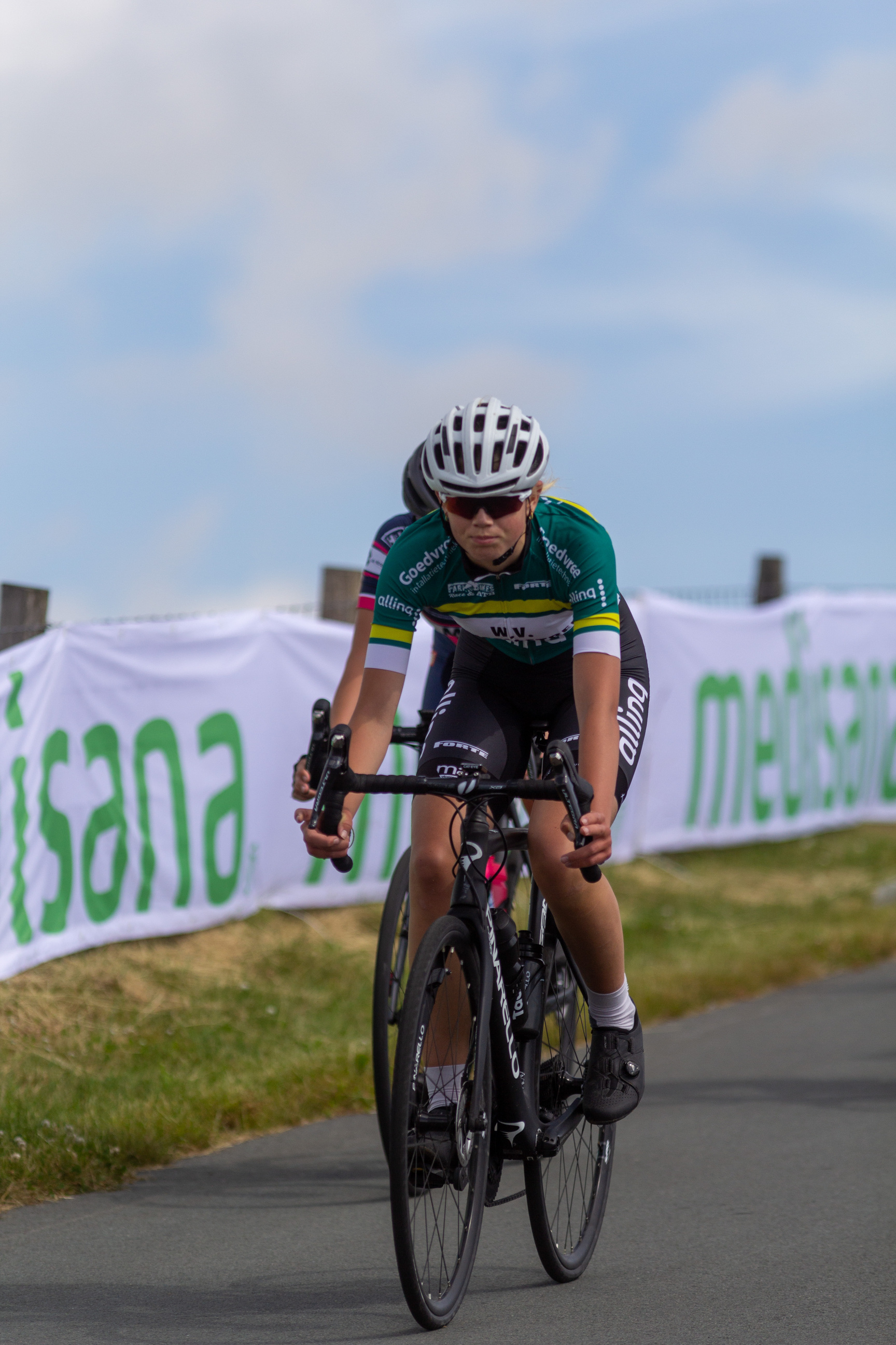 A woman is wearing a white and green jersey while riding her bicycle.