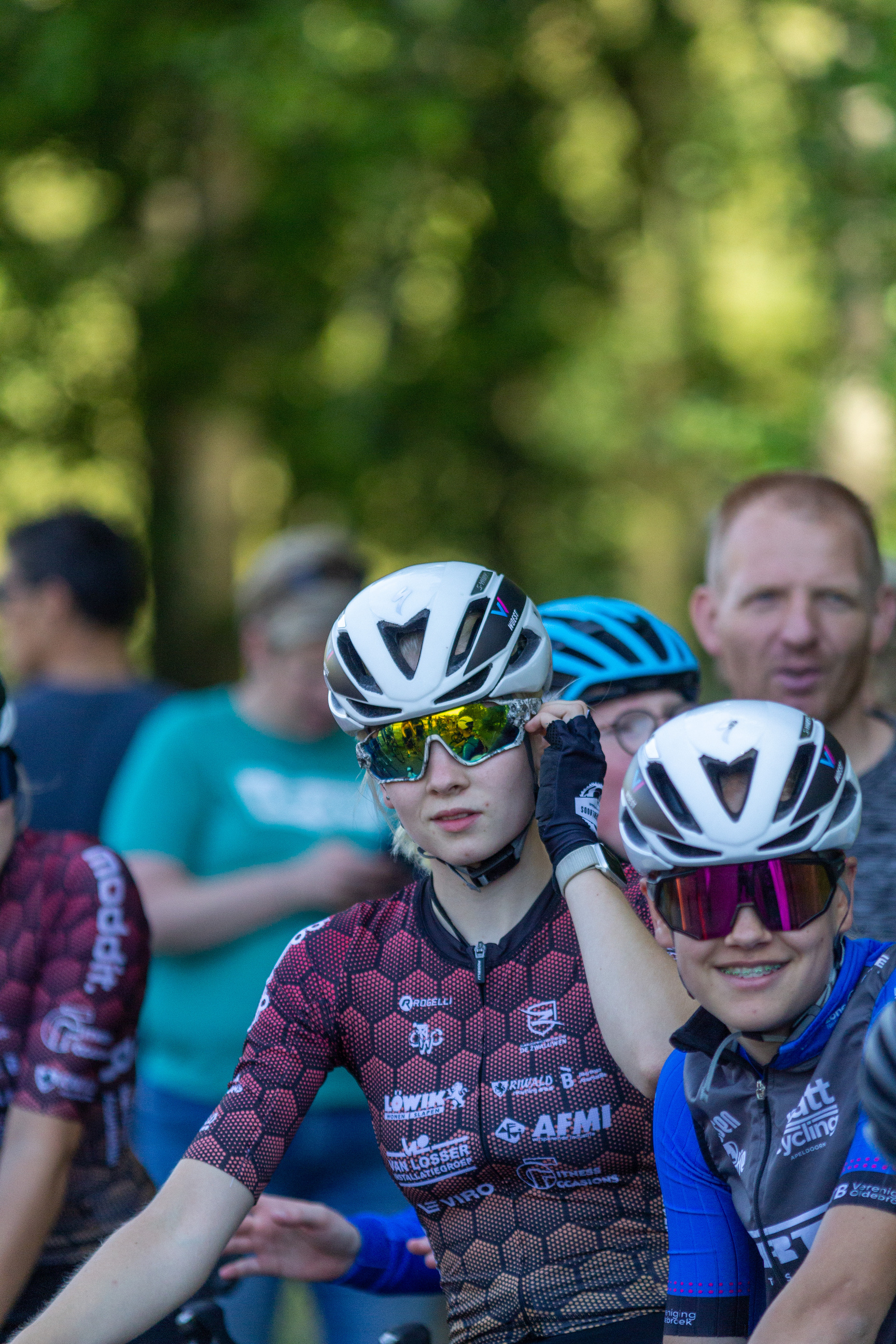 A group of people on their bikes, one with a pink jersey says "Nouwe" on it.