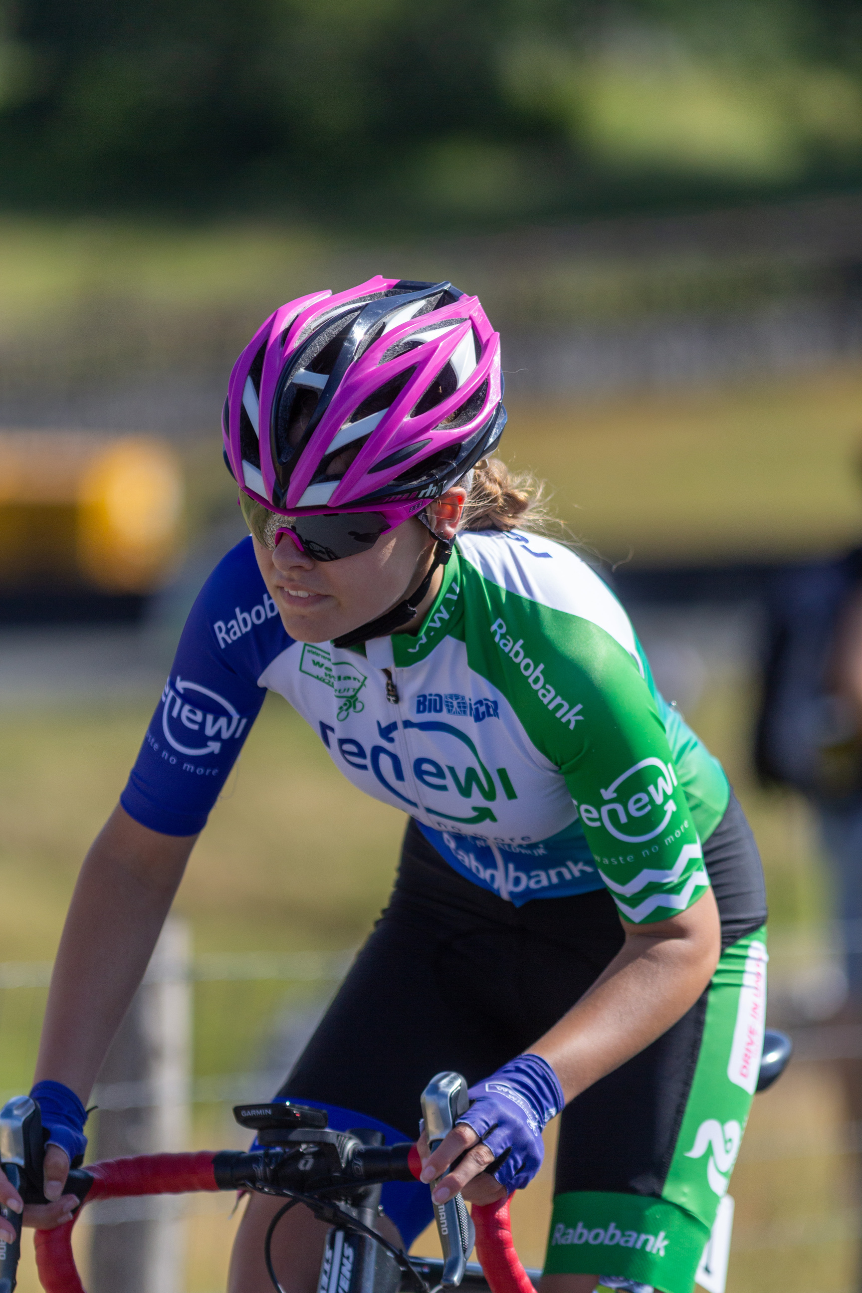 A woman in a blue and green jersey with the number 2 on it is wearing a pink helmet.