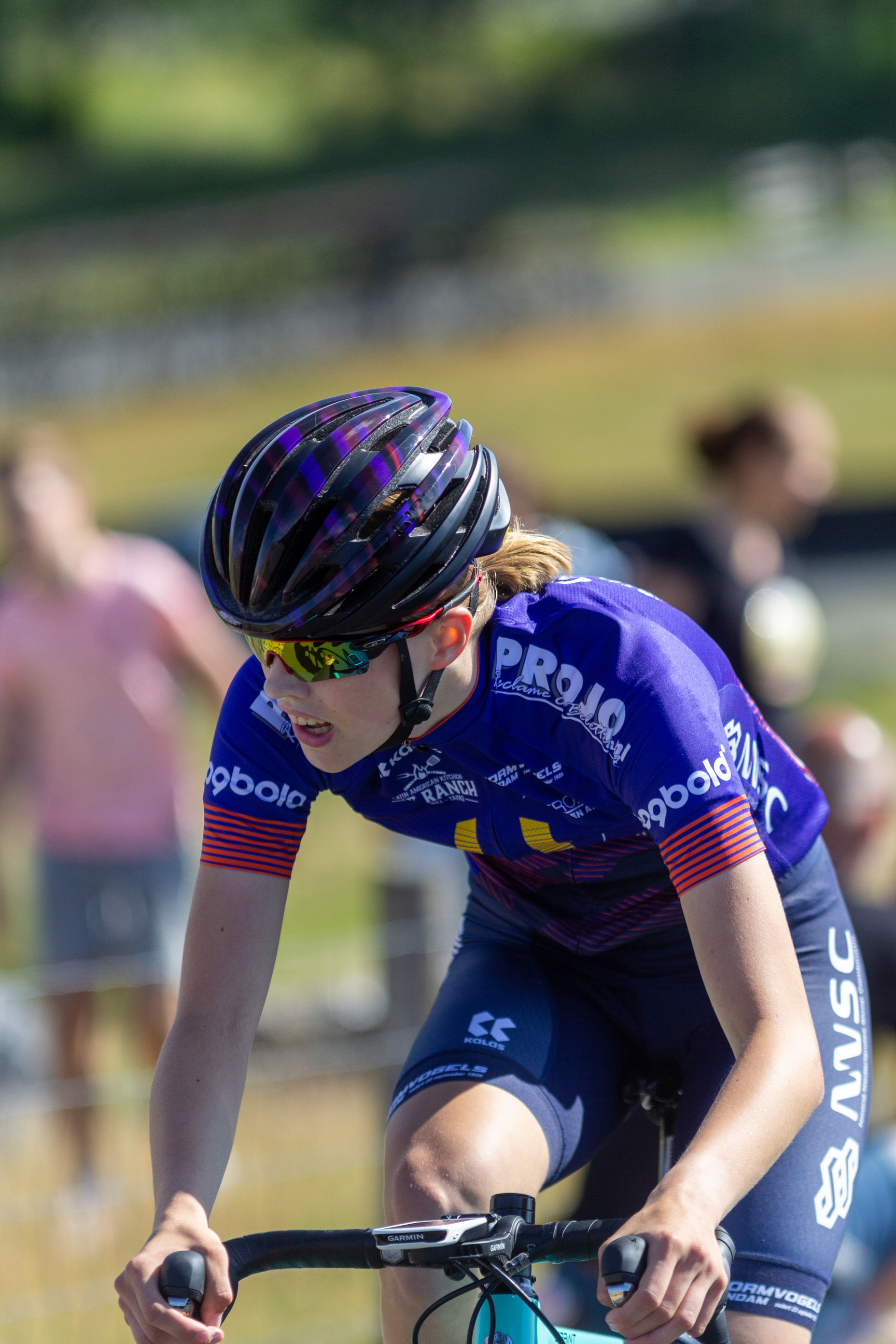 A cyclist in blue jersey with letters on it, races on the track.