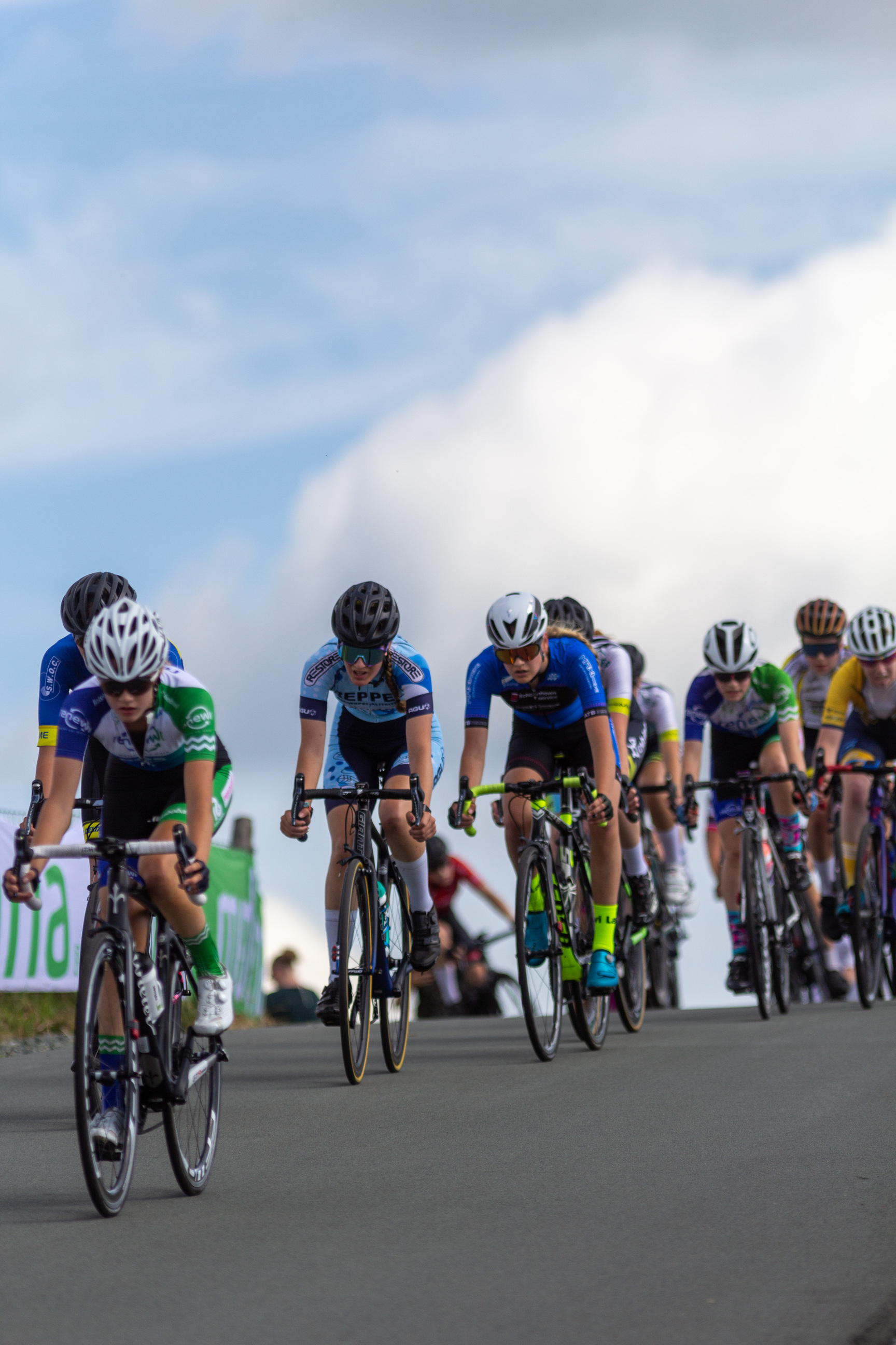 A group of cyclists on a road with 2022 Wielrennen signs on the side.