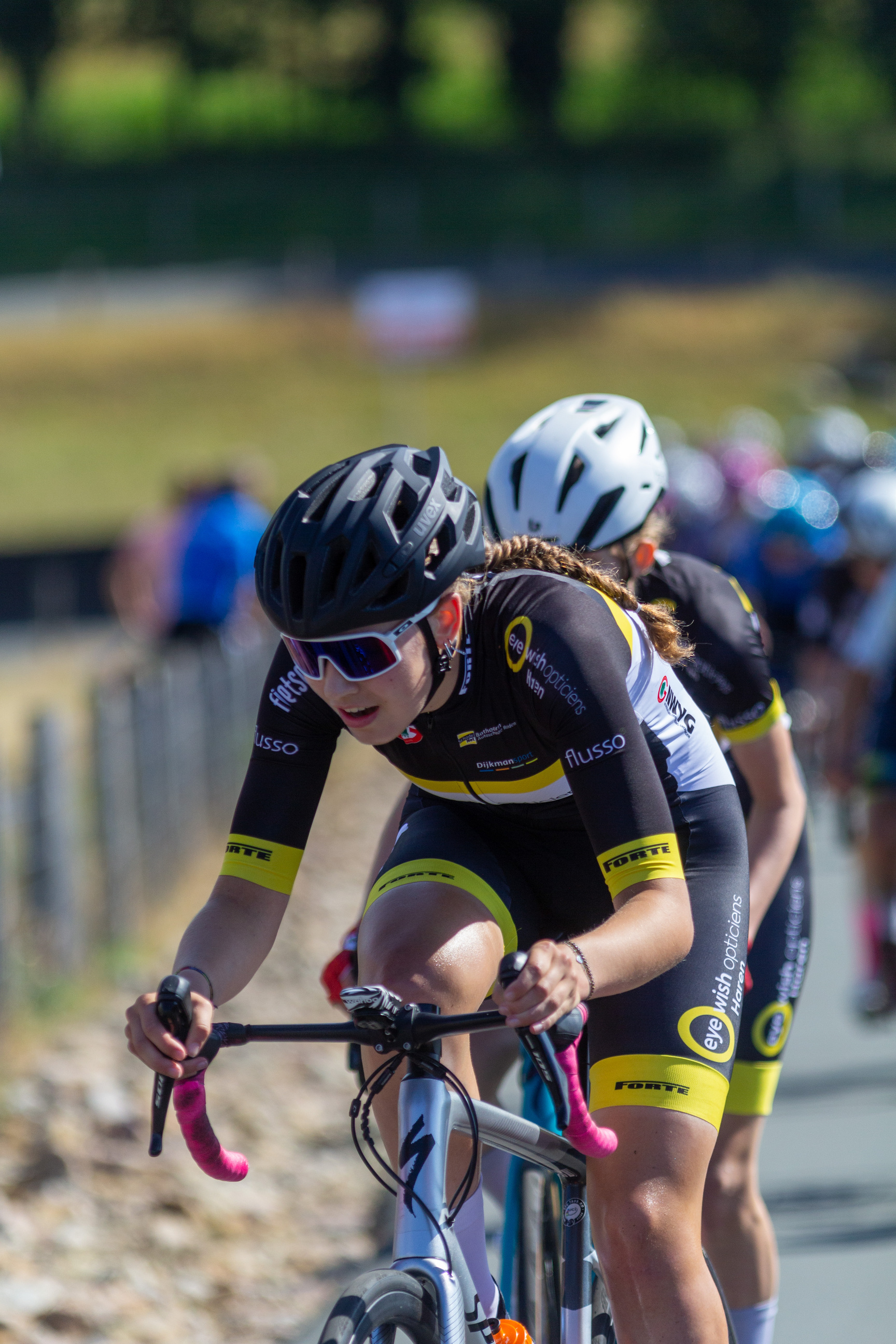 Two women on bicycles are wearing matching uniforms.