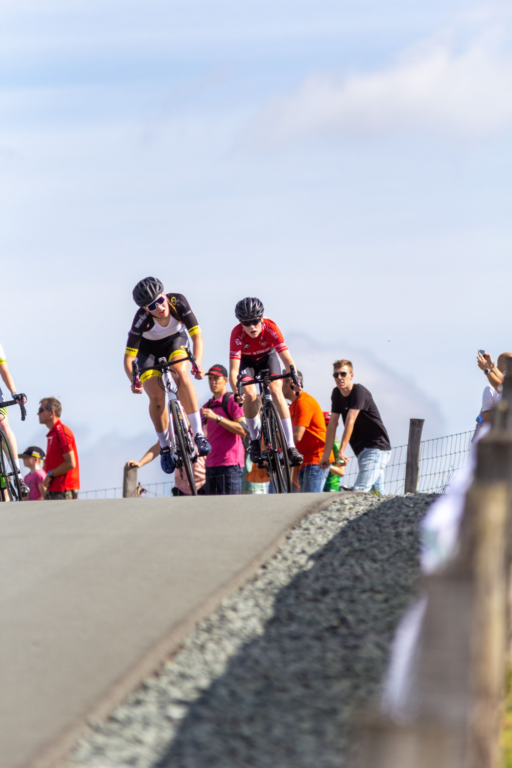 Two cyclists riding on a road next to a crowd of spectators.