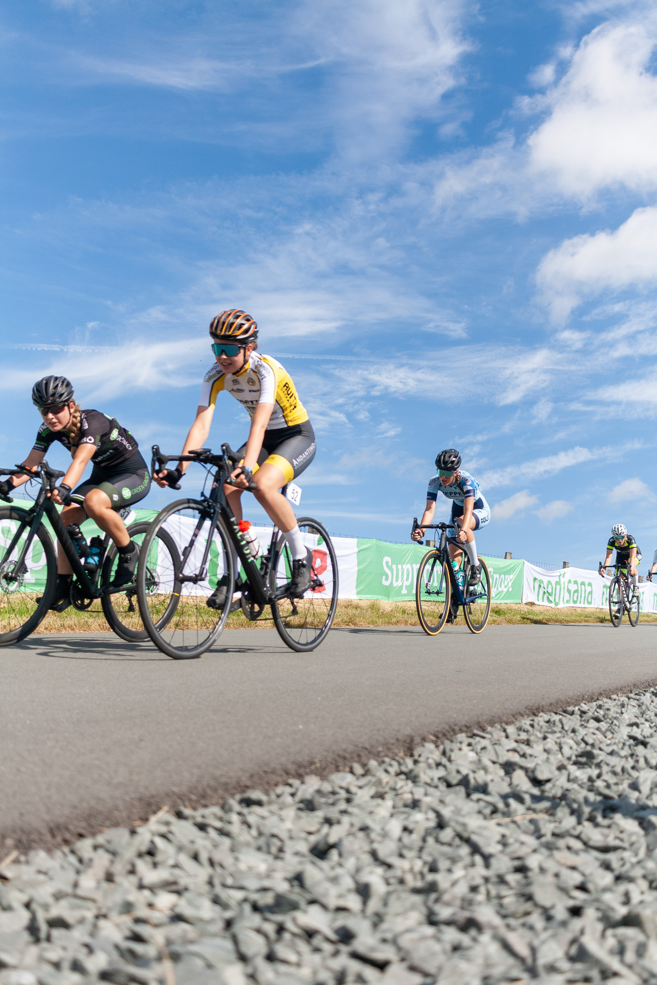 A group of cyclists race down a road on a sunny day.