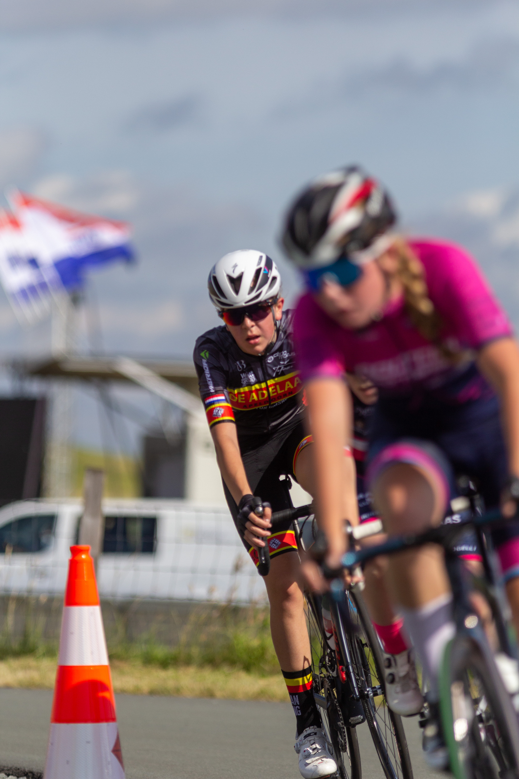 A cyclist wearing a black and orange jersey is racing with other cyclists on the street.