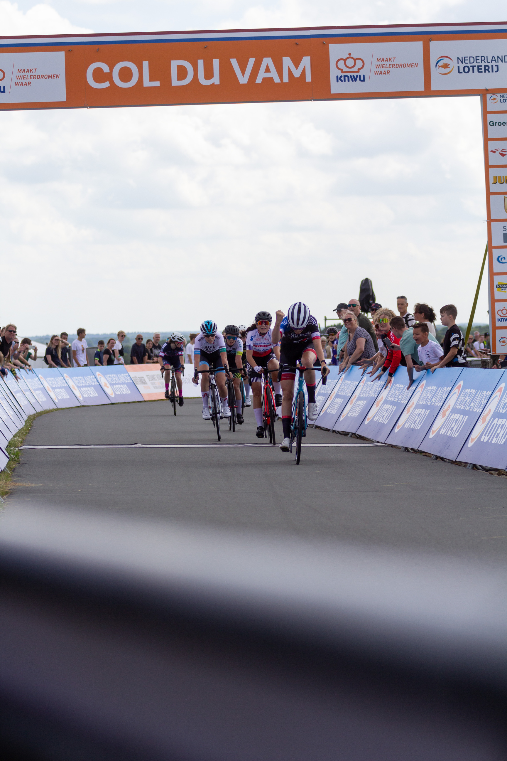 A group of cyclists race across the finish line at a track event.