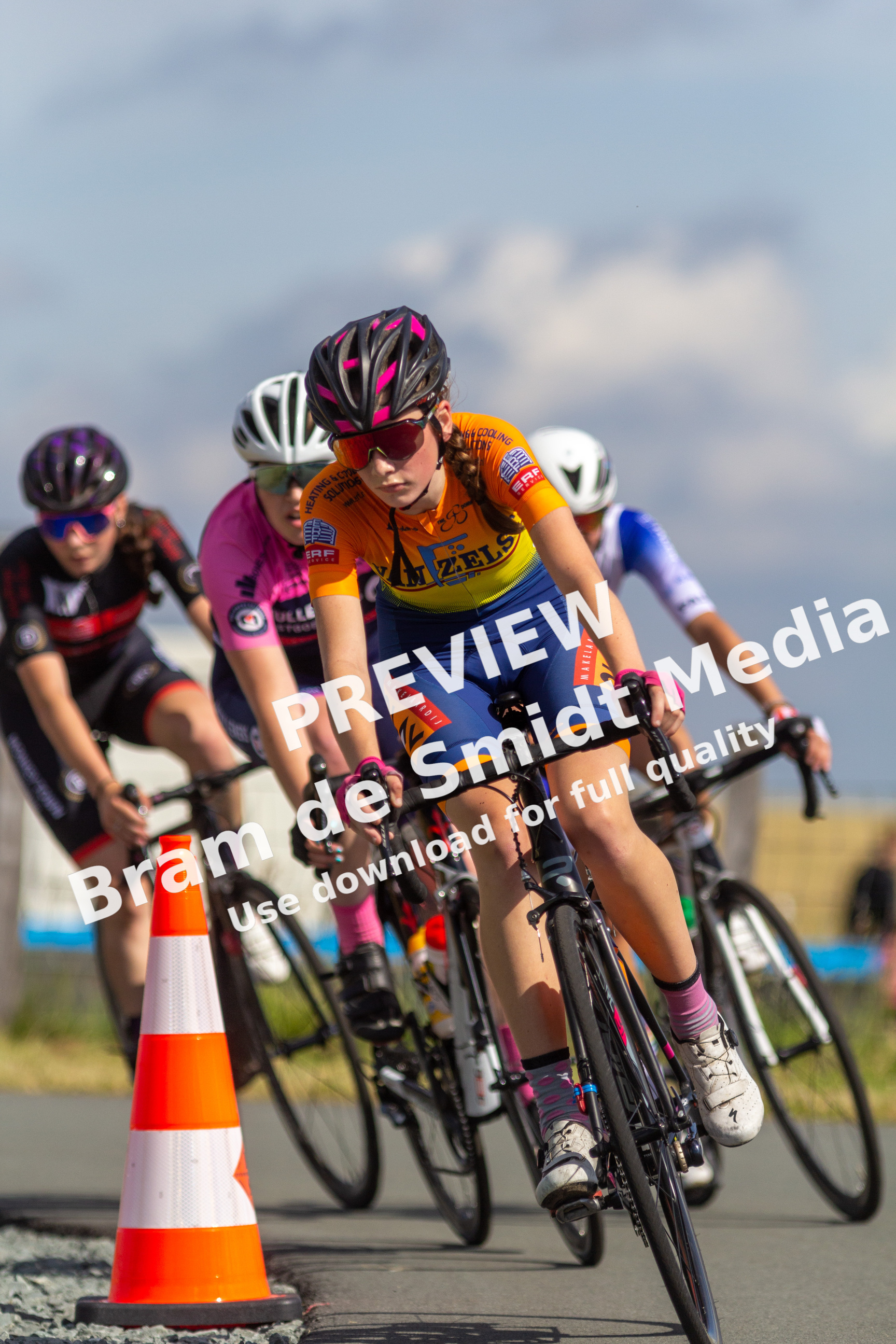 Four women wearing helmets, one of them with a pink helmet, race on their bikes.