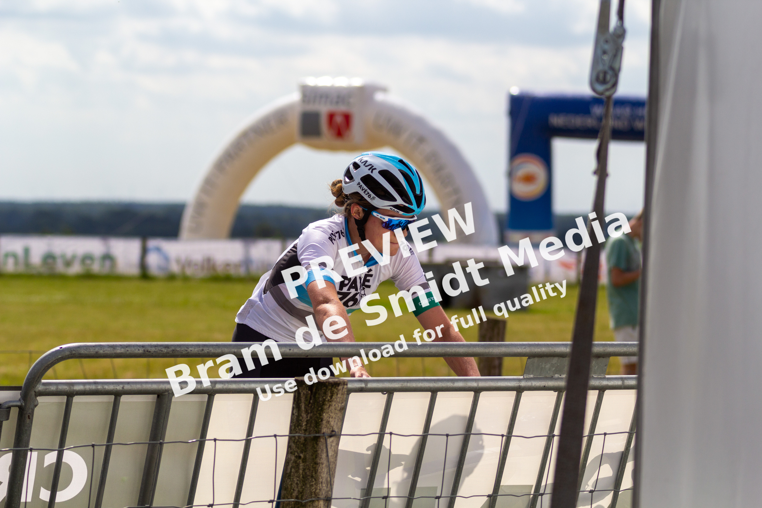 A woman wearing a helmet and riding a bike. She is at the starting line of a bike race.