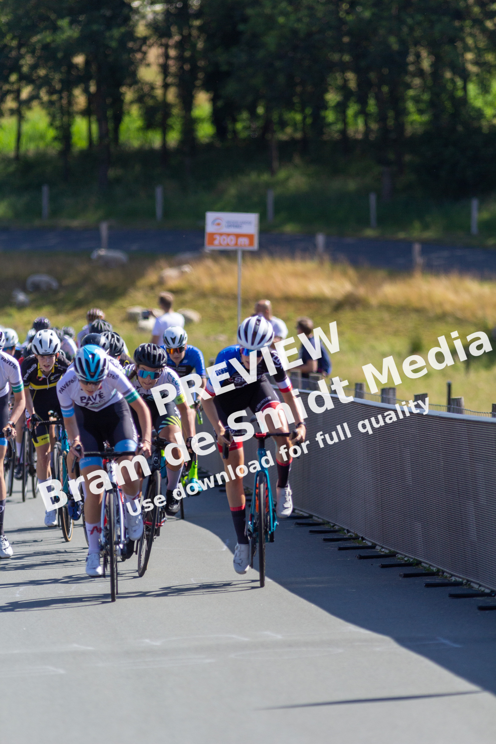 A group of cyclists are riding down a road with a sign behind them that reads 2022.