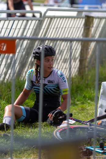 A girl wearing a white and blue top, sitting on the grass near her bicycle with the word "Nacht" written on it.