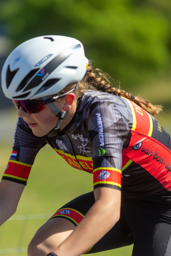 A woman on a bike is wearing a shirt that says "NK Dames" and "Wielrennen".