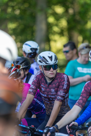 A cyclist in a black and red outfit has the letters "B" on her helmet.