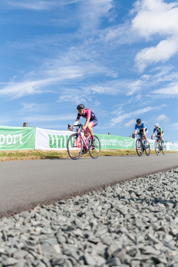 Four cyclists racing down a road with the word "UNILEI" in the background.