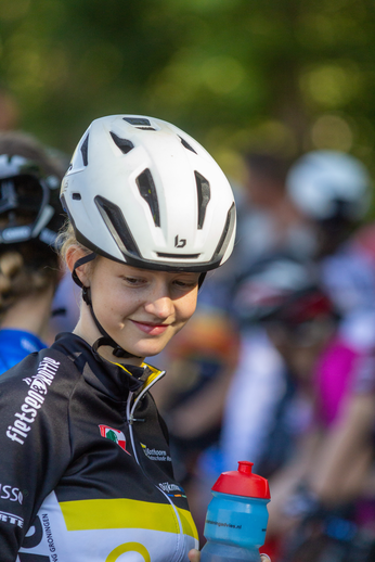 A female cyclist is wearing a helmet and holding a water bottle.