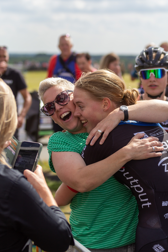 Two women hug each other with one wearing a shirt that says BIKOUT.