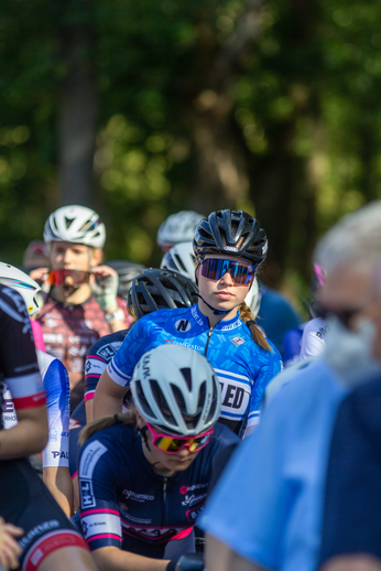 A group of cyclists, dressed in blue and white uniforms, are riding through a park.