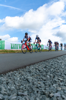 Several cyclists riding on the side of a road near a sign that says "UNIVERS".