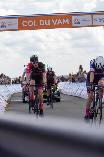 Three bikers are racing to the finish line at a race sponsored by Col du Vam.