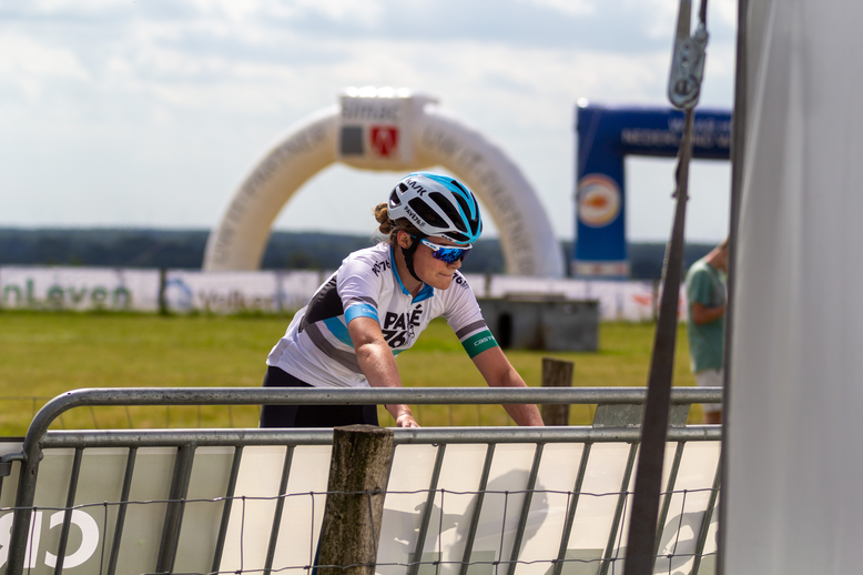 A woman wearing a helmet and riding a bike. She is at the starting line of a bike race.