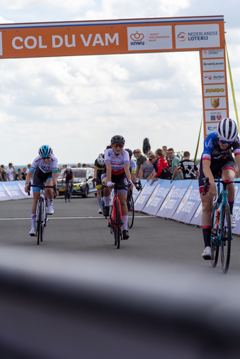 Four cyclists racing down a track, with the word "Col du Vam" in the background.