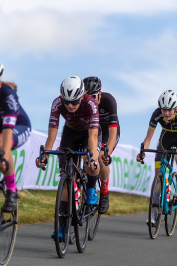 Bike racer's wearing black helmets and glasses are seen riding along a road.