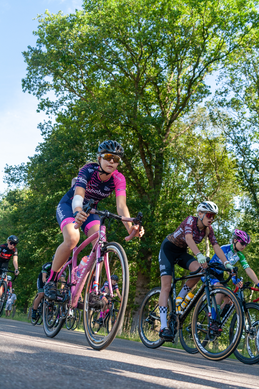 A cyclist wearing a pink helmet on her head and a purple shirt is riding a pink bike down the street.