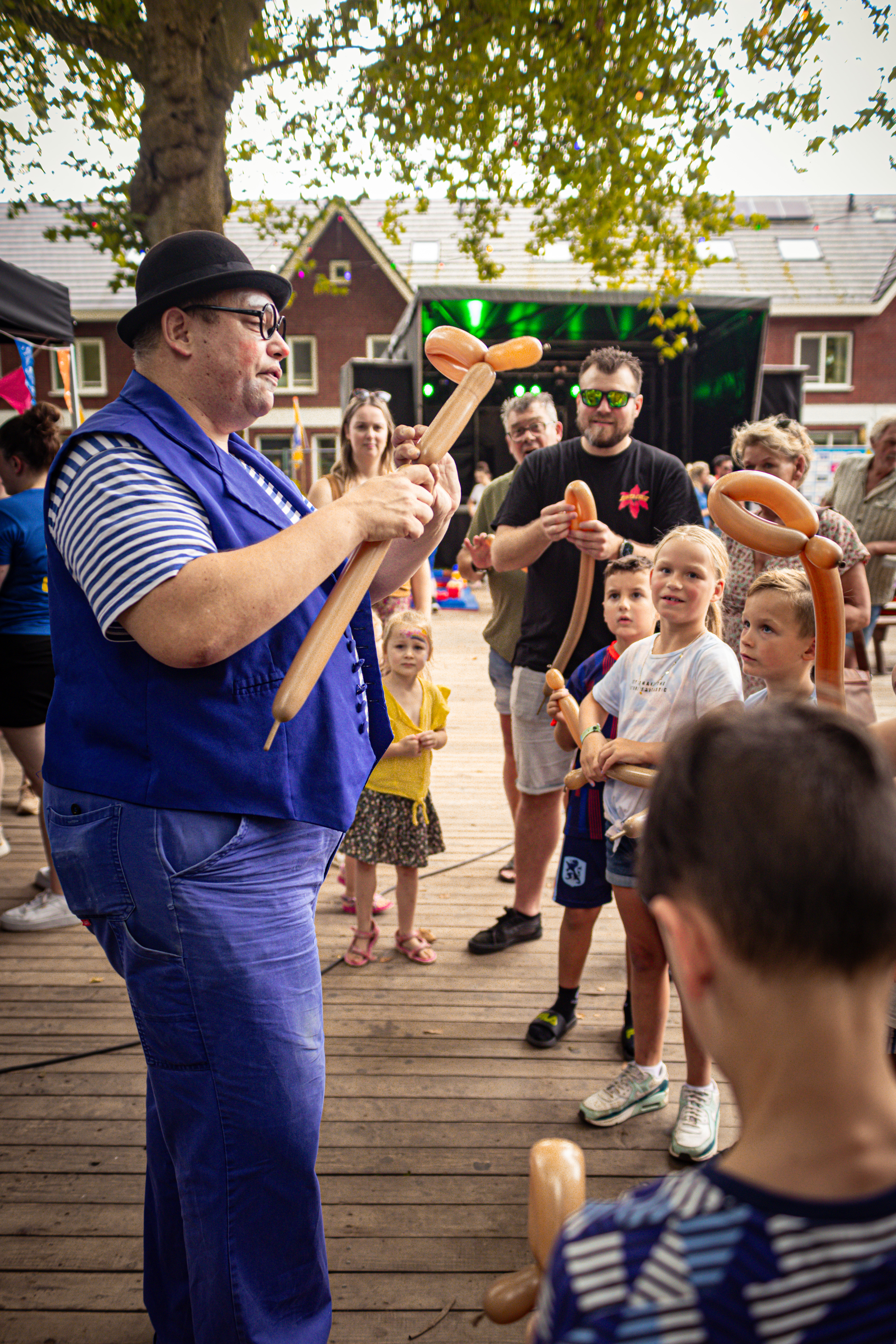 A man wearing a blue outfit and a black hat holds two brown pretzels in front of a group of children.