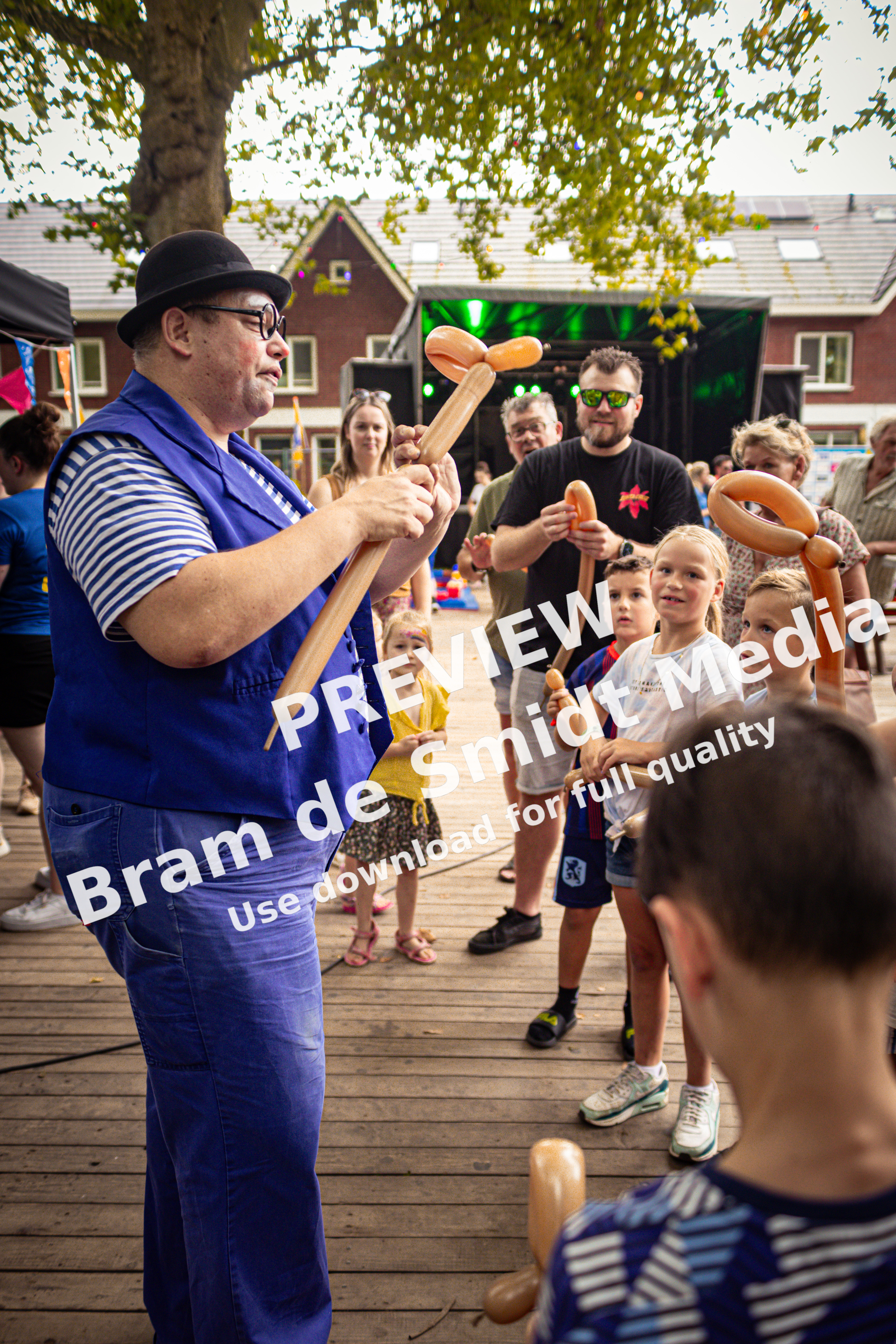 A man wearing a blue outfit and a black hat holds two brown pretzels in front of a group of children.