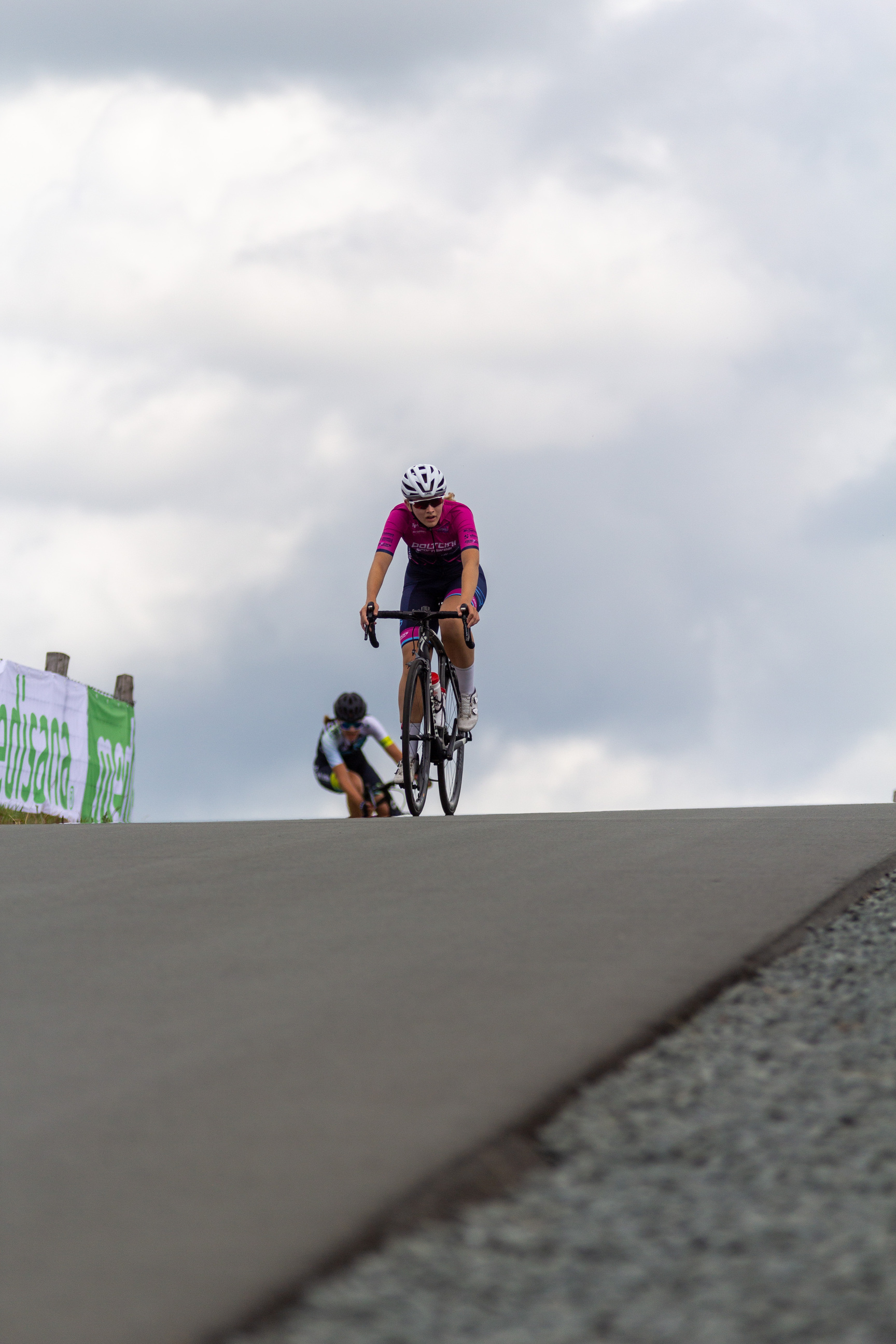 Two cyclists on a road with the word "Wielrennen" to their left.