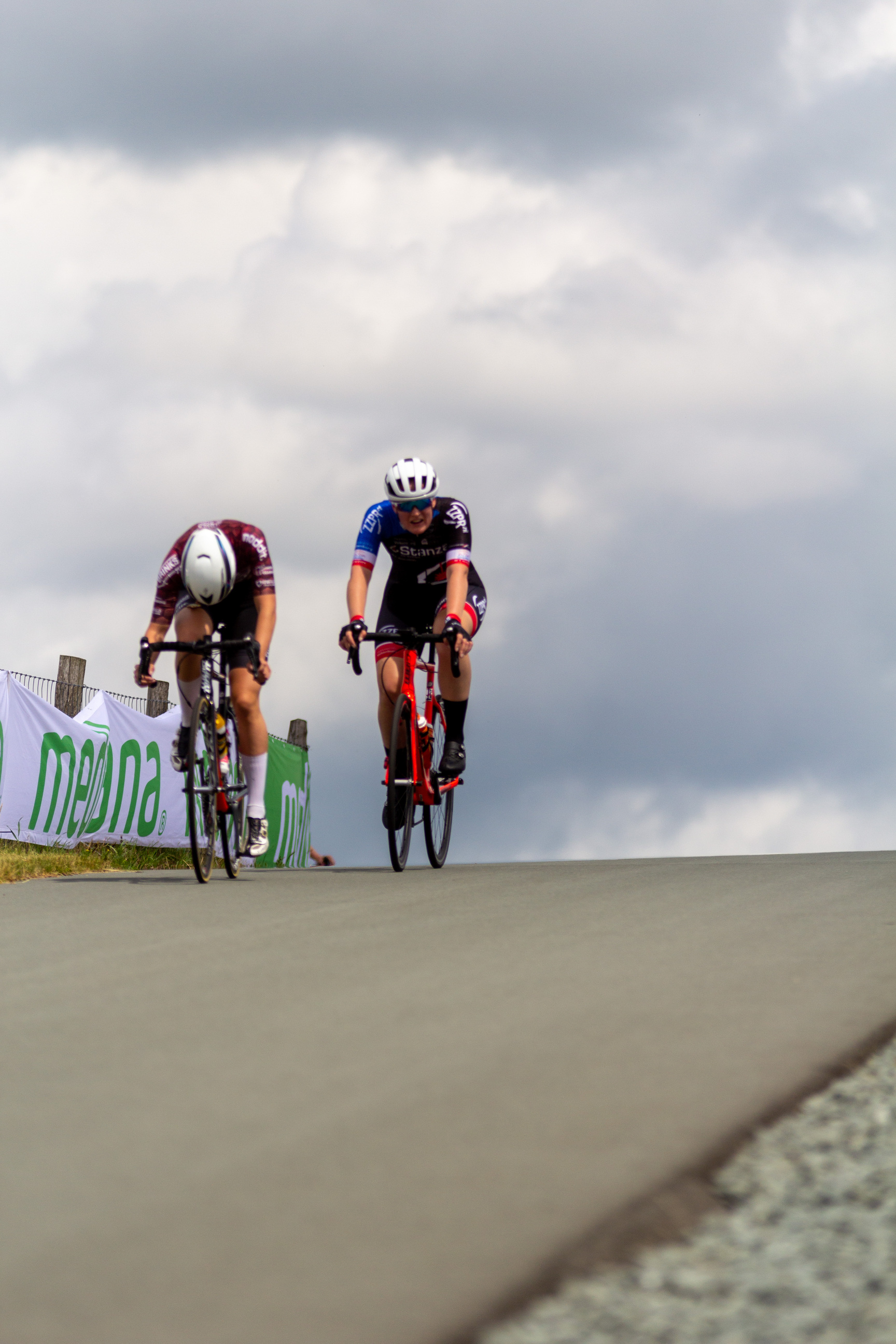 Two cyclists are racing down a road. One of them is wearing a helmet.