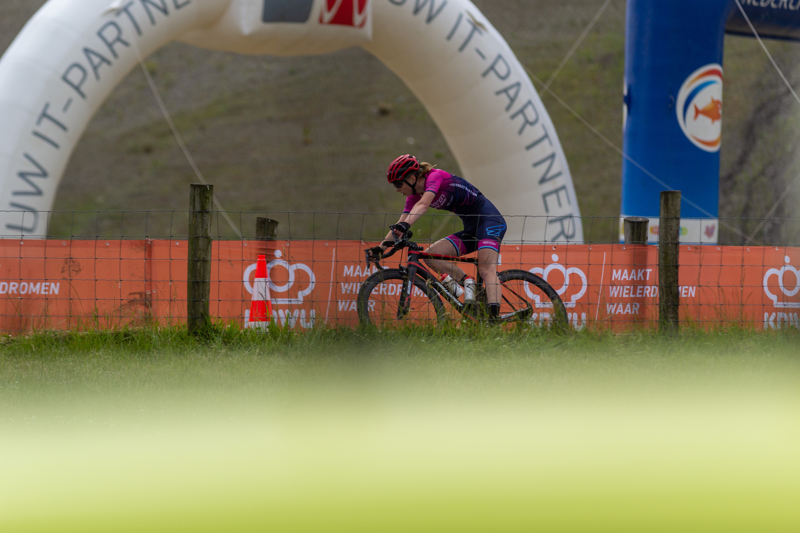 A woman is riding a bike in the Wielrennen race. She is wearing a purple and black shirt with number 4 on her back.