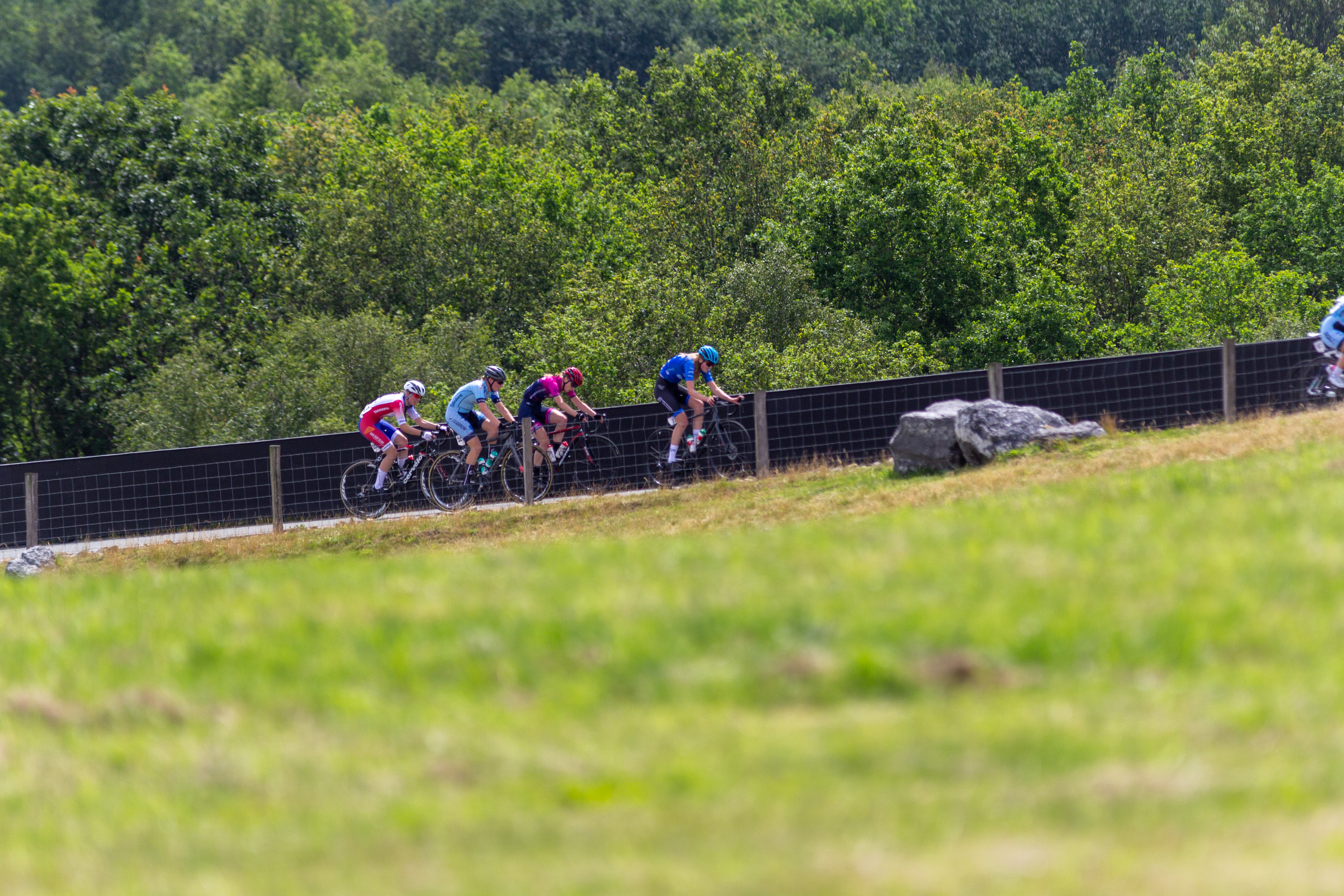 A group of cyclists, including some wearing a pink jersey, race on a track.