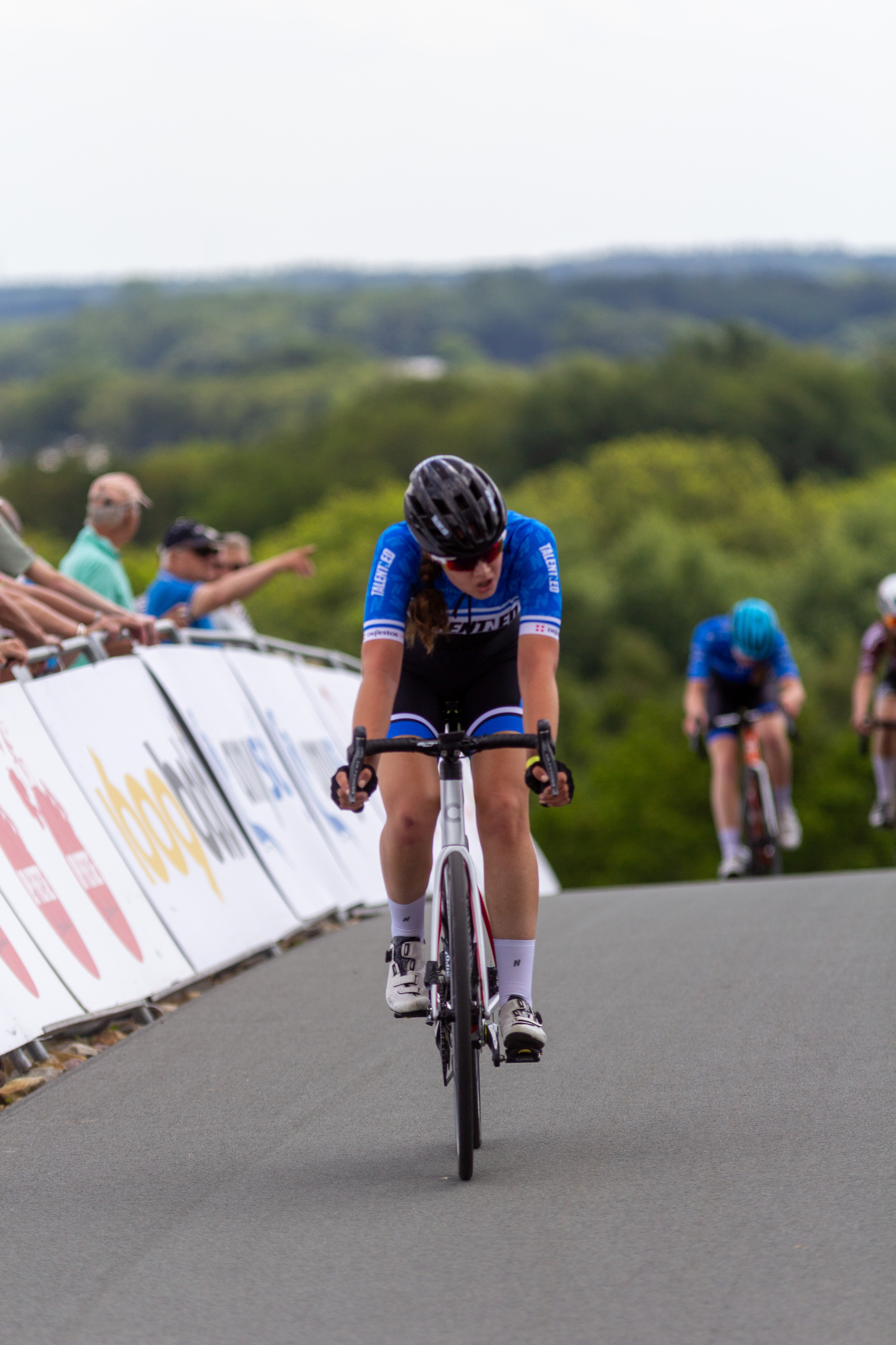 A female cyclist wearing a blue shirt and white shorts riding her bicycle.