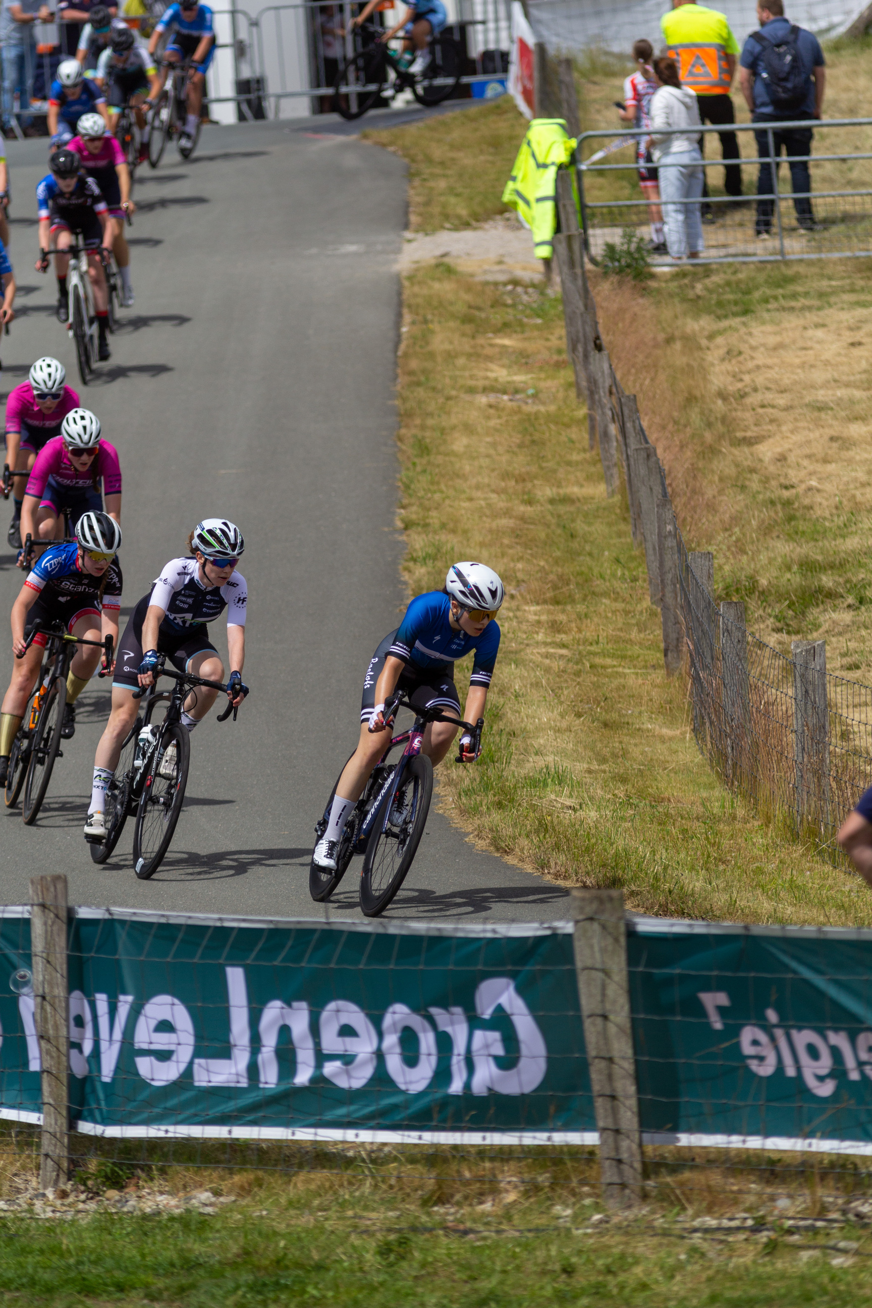 A group of cyclists race on a track with a banner that reads "Junioren Dames".