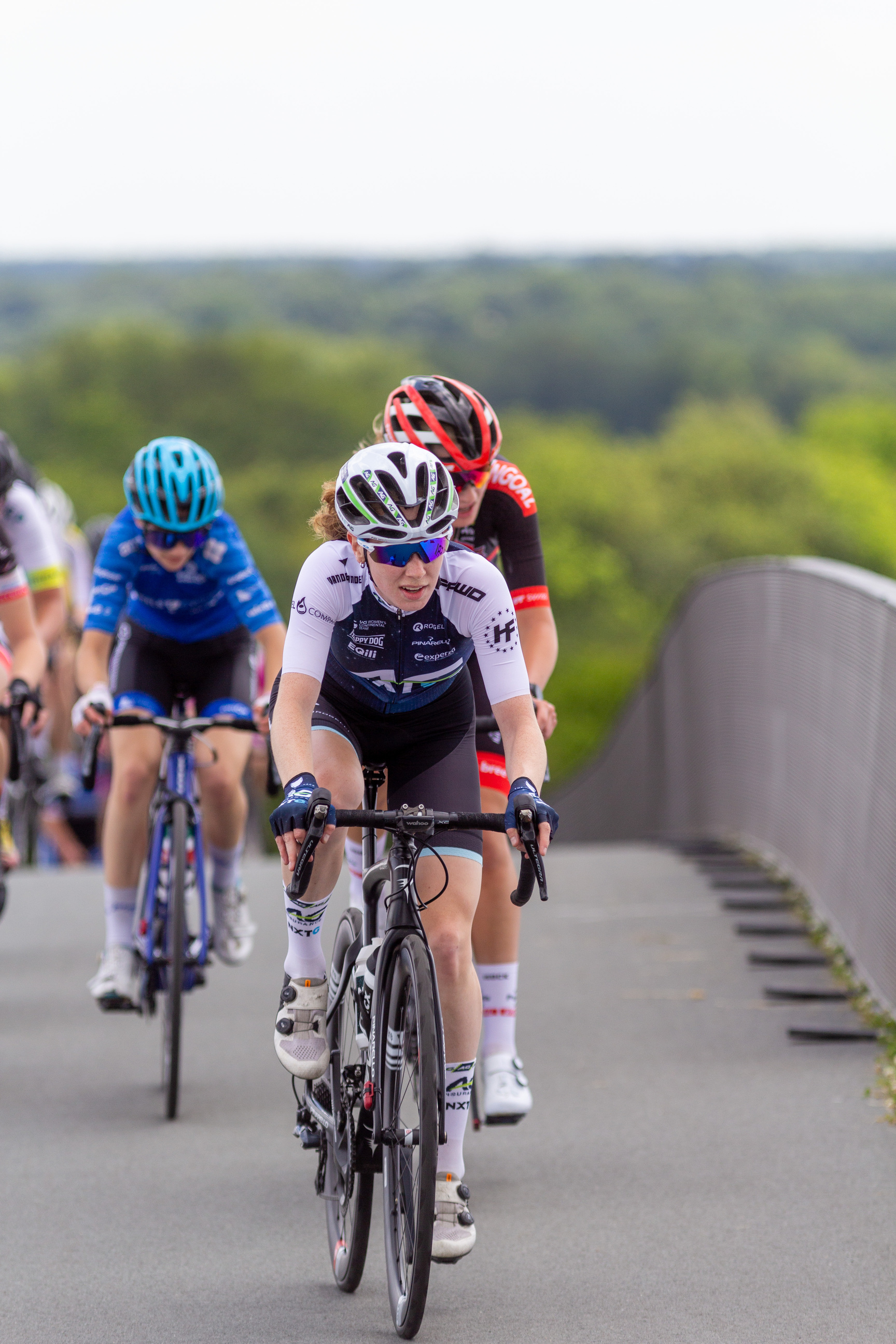 A group of cyclists are racing on a road with trees in the background.