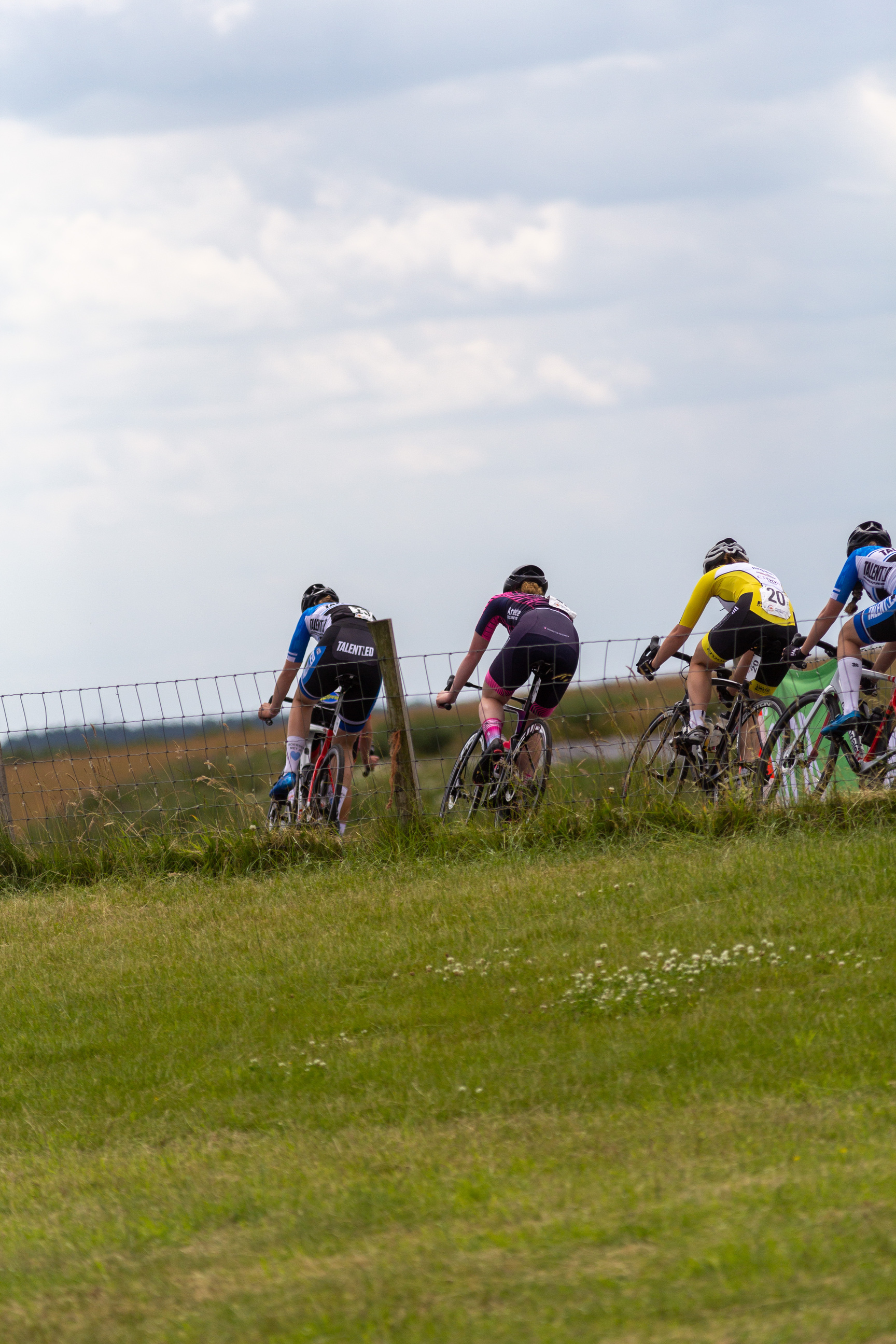 Three cyclists riding on a grassy field with one of them wearing the number 6 on her jersey.