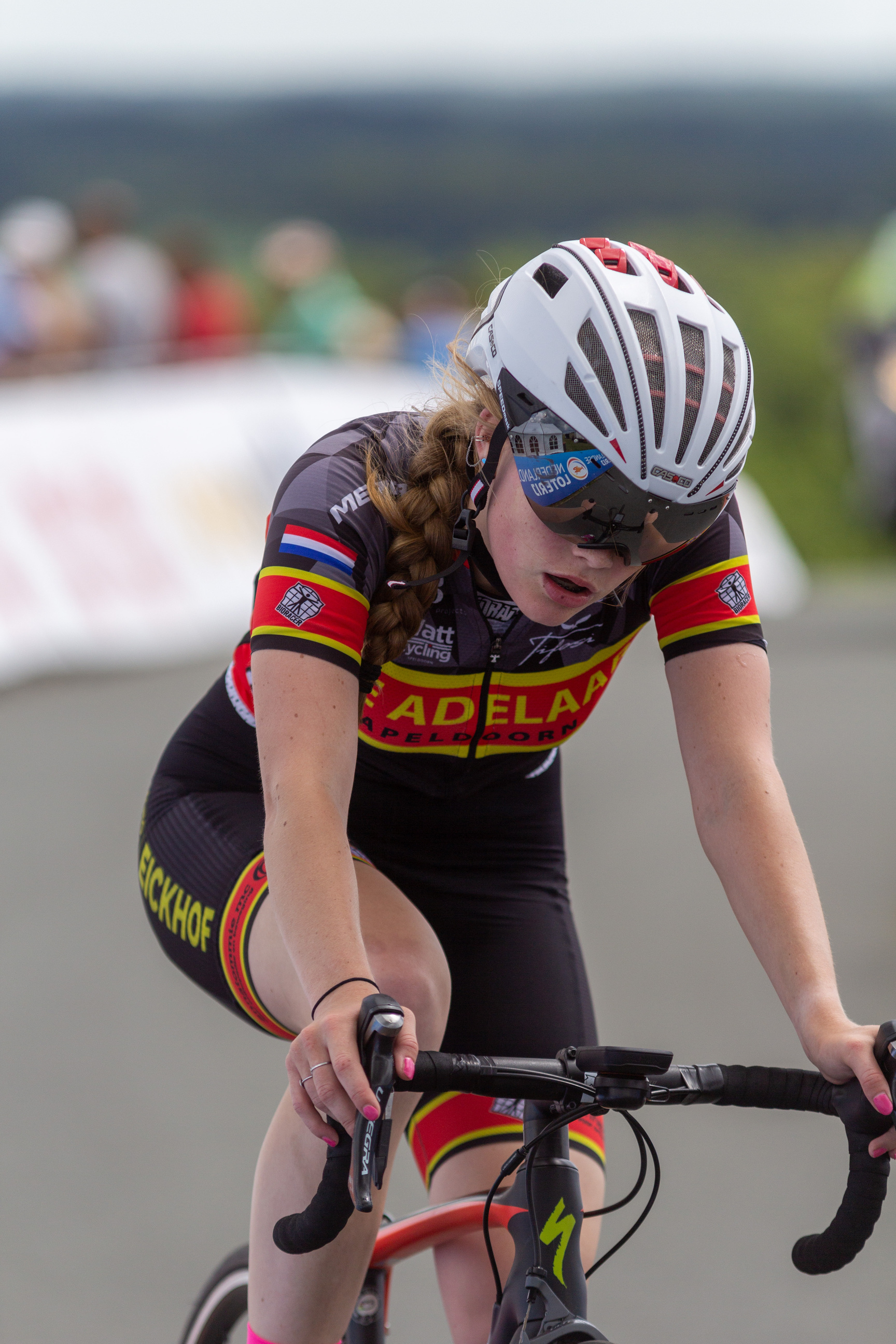 A young woman on a bicycle. She is wearing red and black clothing with Adela written on the chest.