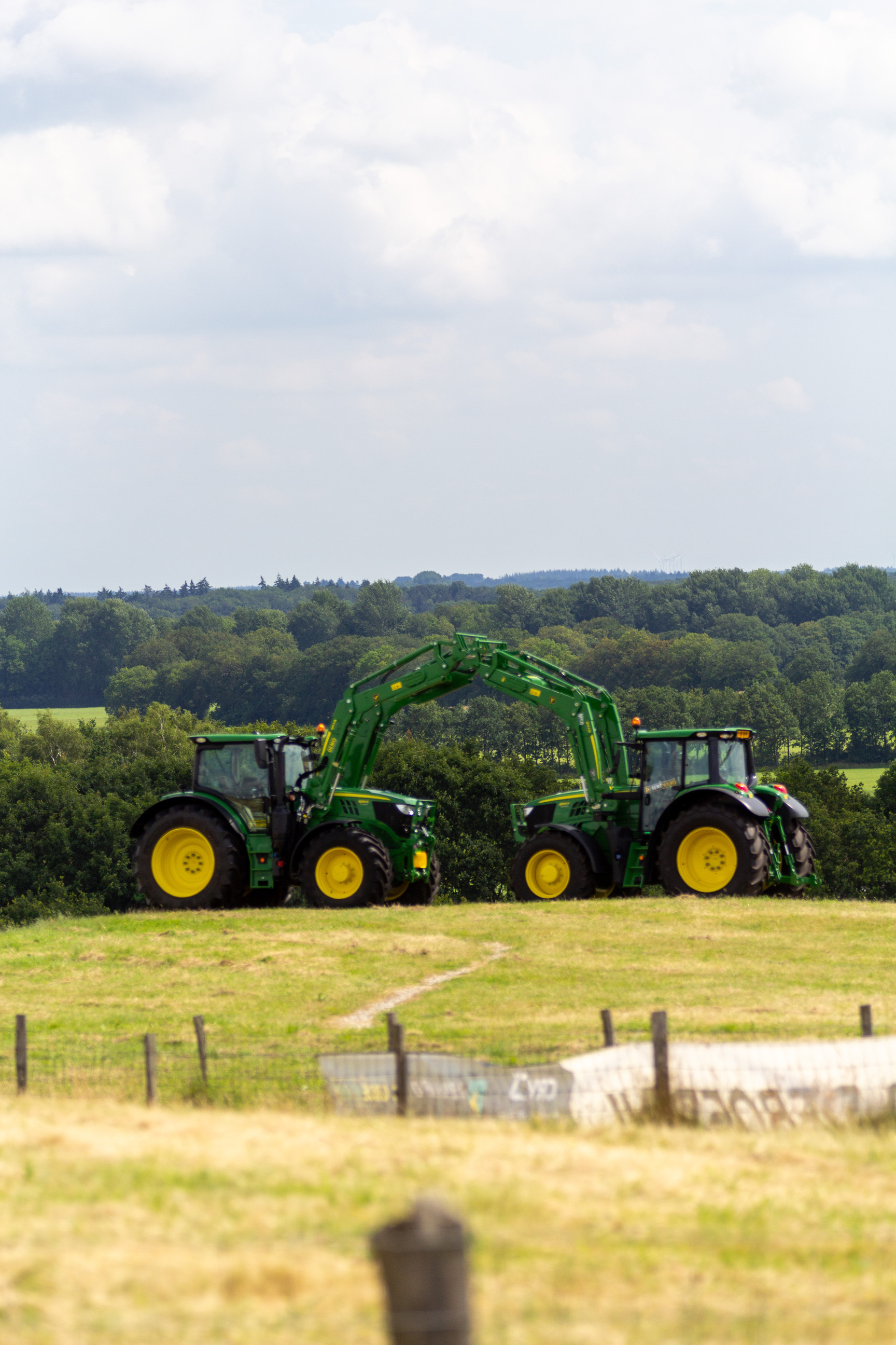 Two green tractors with a yellow wheel sit on a grassy field.