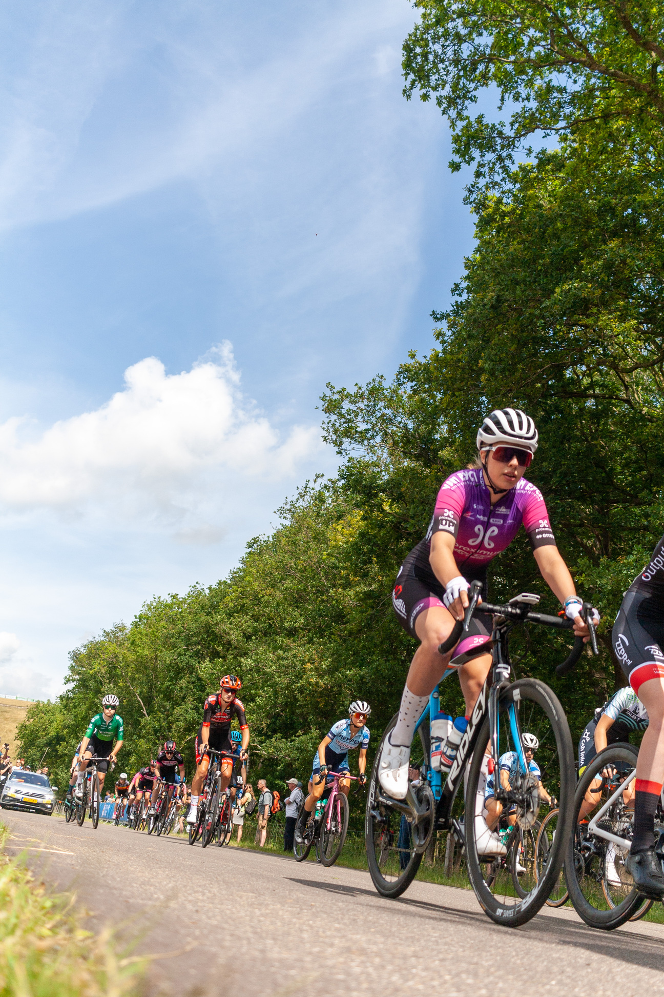 A group of cyclists are riding on a street, with one person wearing a pink shirt.