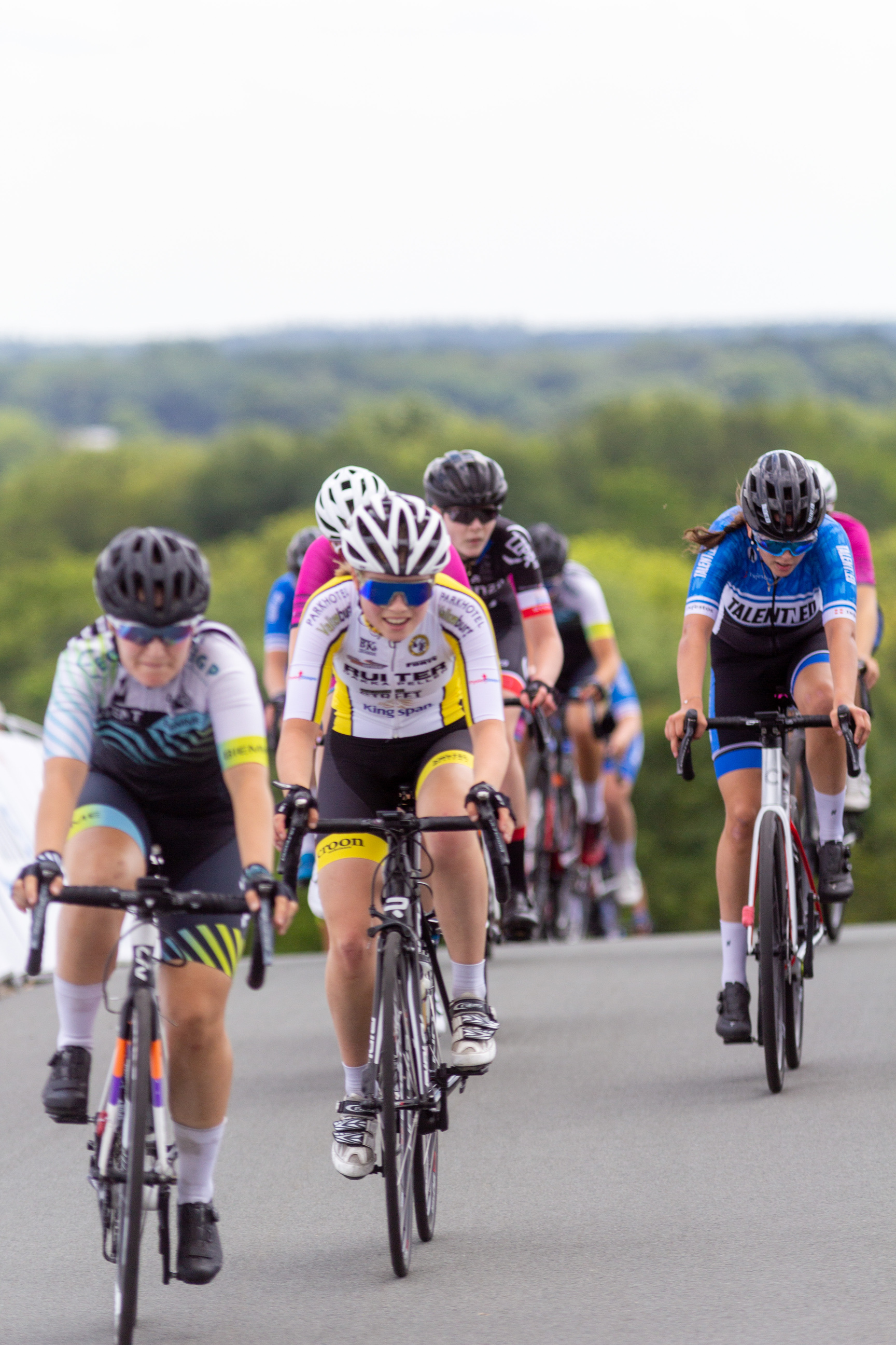 A group of cyclists are wearing blue and black shirts that say NK Dames on them.