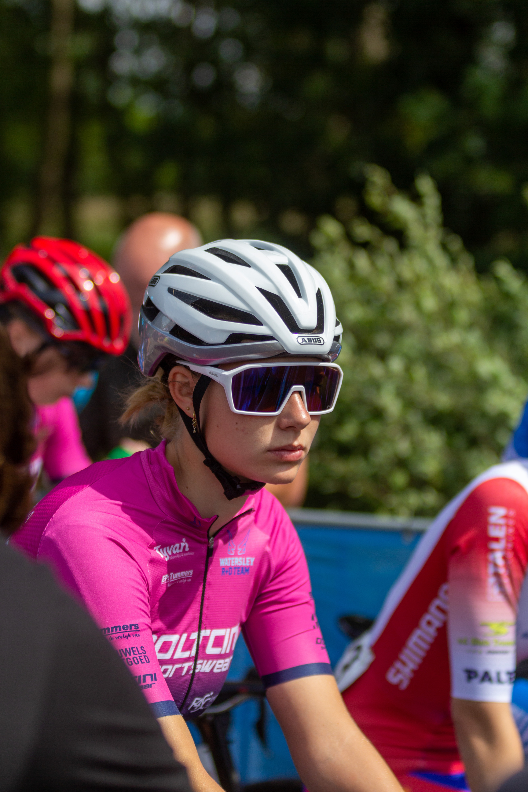 A woman in a pink jersey with the word "Dames" on it is riding a bicycle.