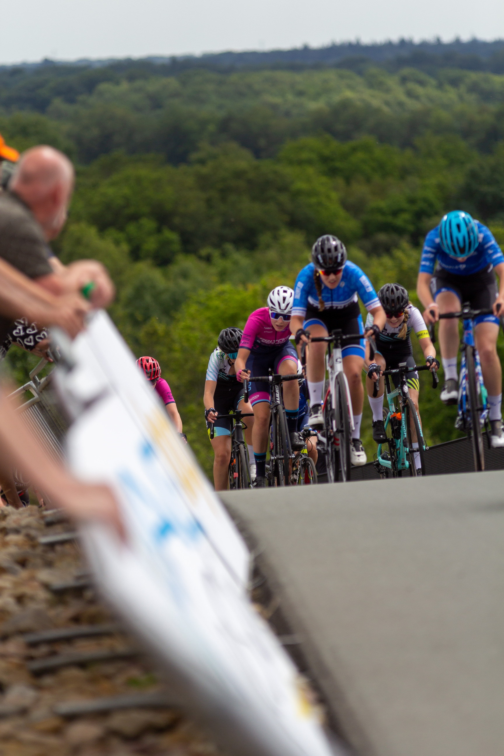 A group of 6 cyclists are racing at a track, and the track is sponsored by NK Dames.