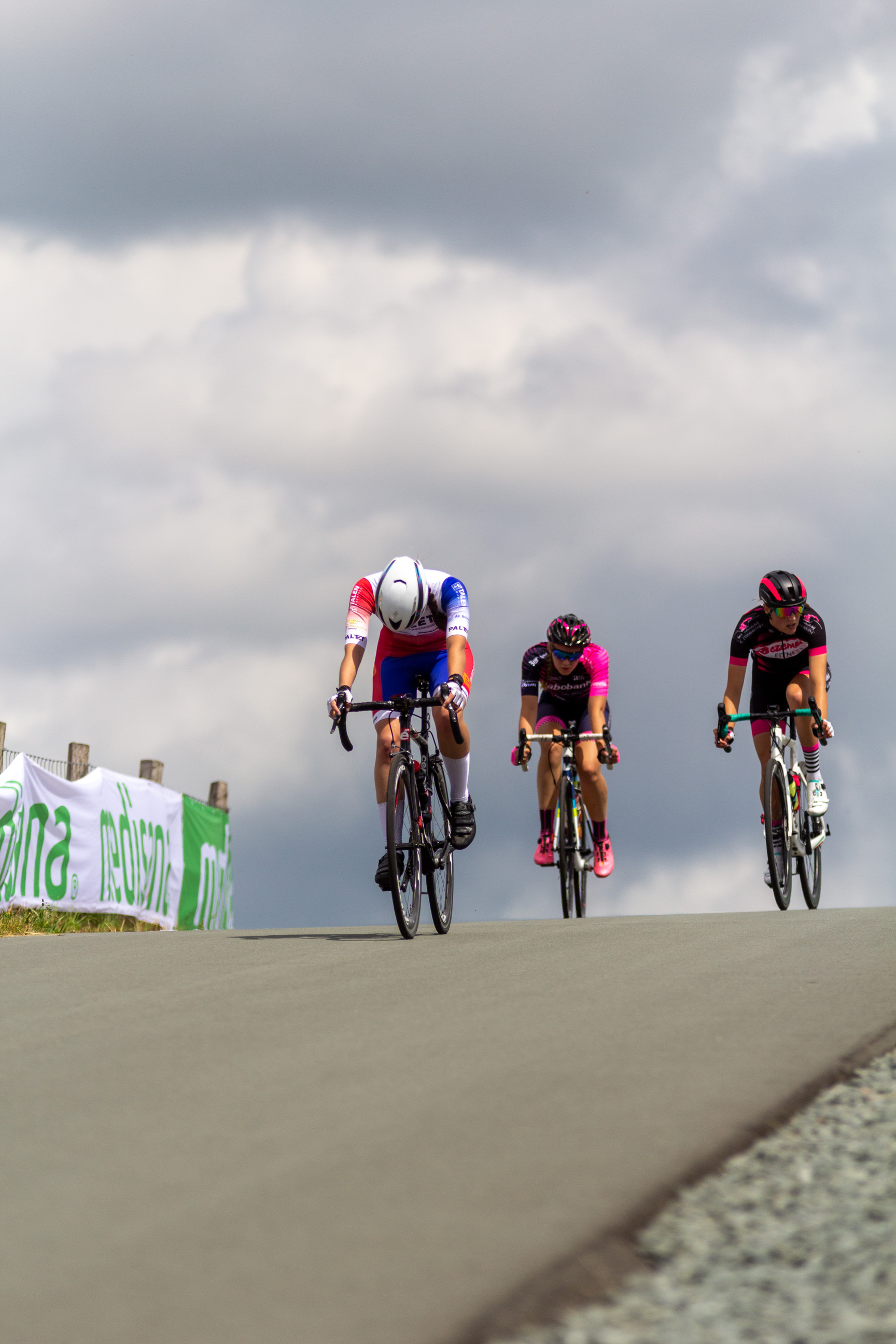 Three cyclists racing on a road with the word "Junioren Dames" in the background.