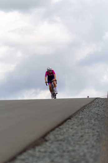 A woman in a pink shirt and white helmet is riding her bike down a hill.