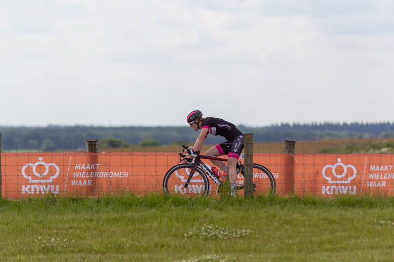 A bicycle racer is riding near a red advertising board that says "KWK".